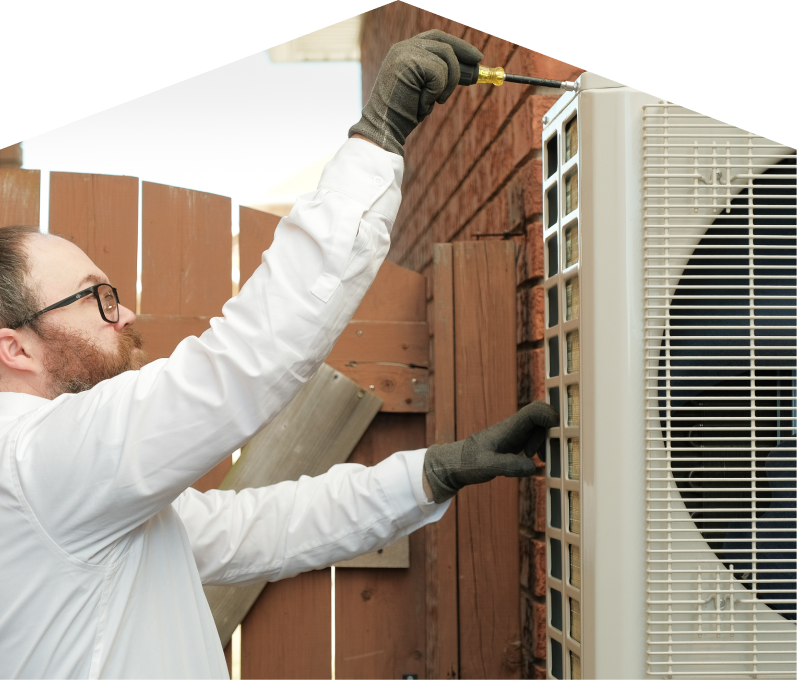 Peel service personnel working on an AC condenser, using a screwdriver to secure the unit’s panel outdoors beside a wooden fence. Peel service personnel working on an AC condenser, using a screwdriver to secure the unit's panel outdoors beside a wooden fence.
