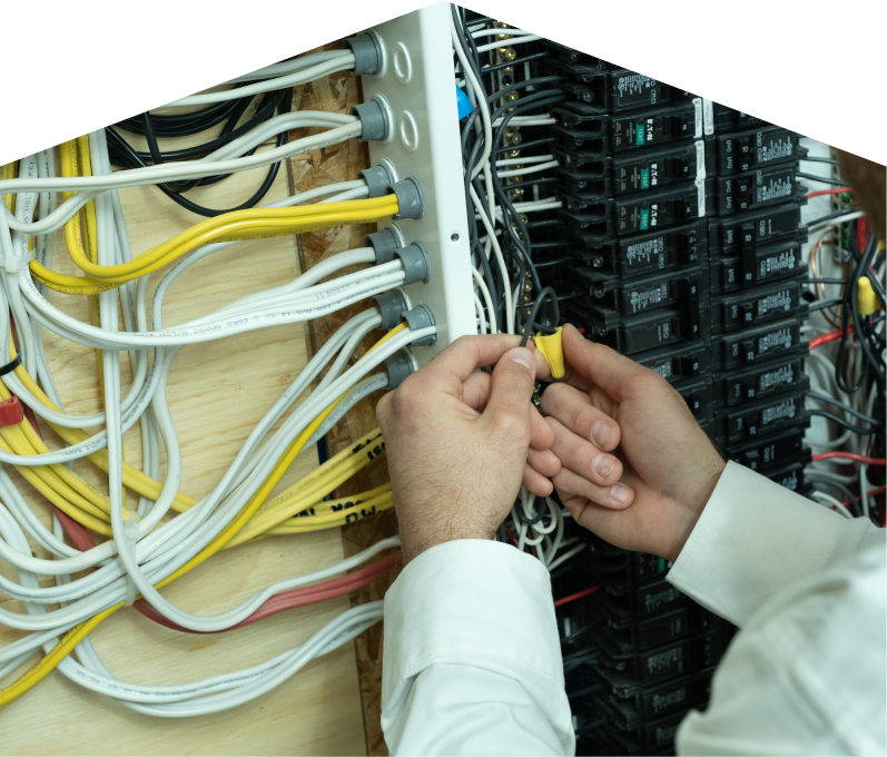 Peel service personnel working on electrical installations, connecting wires inside a residential breaker panel with neatly arranged colored cables on a plywood backing. Peel service personnel working on electrical installations, connecting wires inside a residential breaker panel with neatly arranged colored cables on a plywood backing.