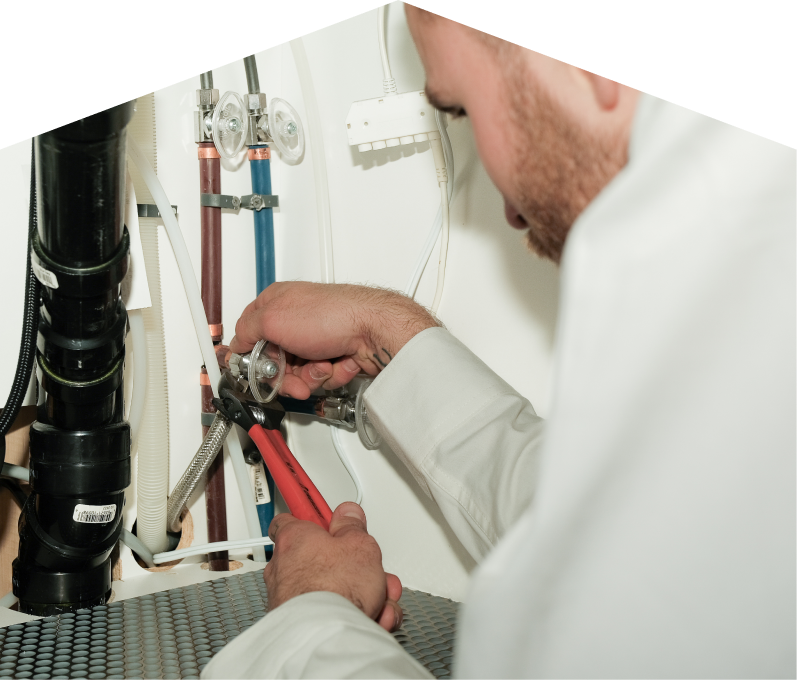 Peel plumbing expert tightening connections under a sink during a faucet installation, surrounded by hot and cold water supply lines and PVC drainage. Peel plumbing expert tightening connections under a sink during a faucet installation, surrounded by hot and cold water supply lines and PVC drainage.