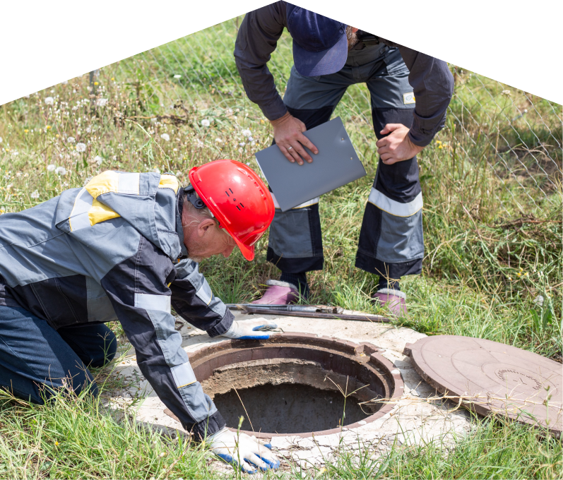 Peel sewer crew inspecting an open manhole in a grassy field, with one member documenting findings on a clipboard. Peel sewer crew inspecting an open manhole in a grassy field, with one member documenting findings on a clipboard.