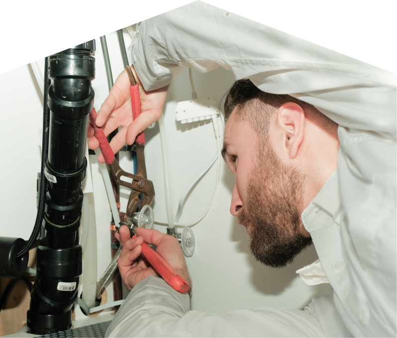 Peel plumbing specialist uses hand tools to tighten pipe fittings beneath a sink during a repair, with visible wiring and drainage lines in the background. Peel plumbing specialist uses hand tools to tighten pipe fittings beneath a sink during a repair, with visible wiring and drainage lines in the background.