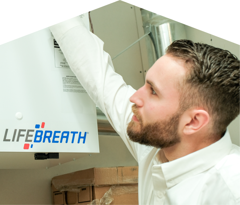 Peel indoor air quality specialist inspects a Lifebreath ventilation unit related to UV air purifiers, with ductwork and boxes in the background. Peel indoor air quality specialist inspects a Lifebreath ventilation unit related to UV air purifiers, with ductwork and boxes in the background.