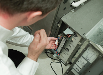 A Peel heating technician inspecting internal wiring during a service check on a residential heating unit. A Peel heating technician inspecting internal wiring during a service check on a residential heating unit.