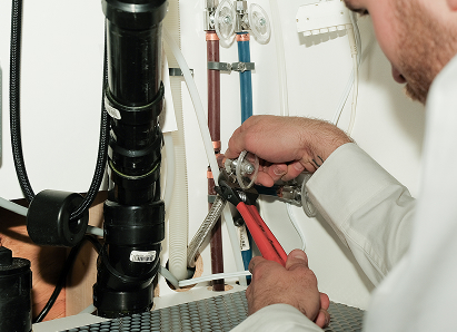 Using two pipe wrenches, a Peel professional plumber services a pipe connection near a vertical flue or vent pipe. Using two pipe wrenches, a Peel professional plumber services a pipe connection near a vertical flue or vent pipe.